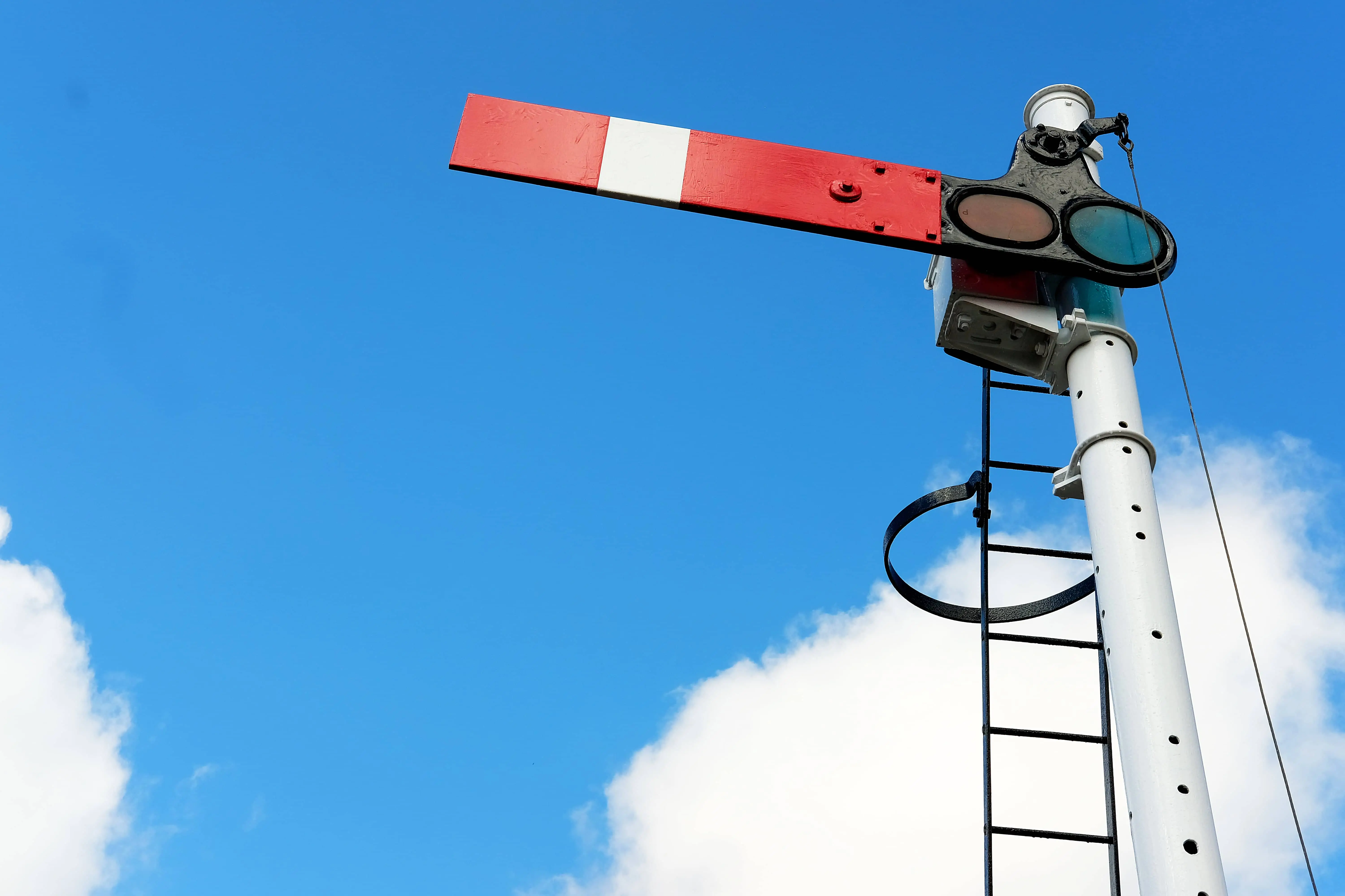 A traditional railway semaphore signal with a red and white arm in the stop position, set against a bright blue sky with scattered clouds