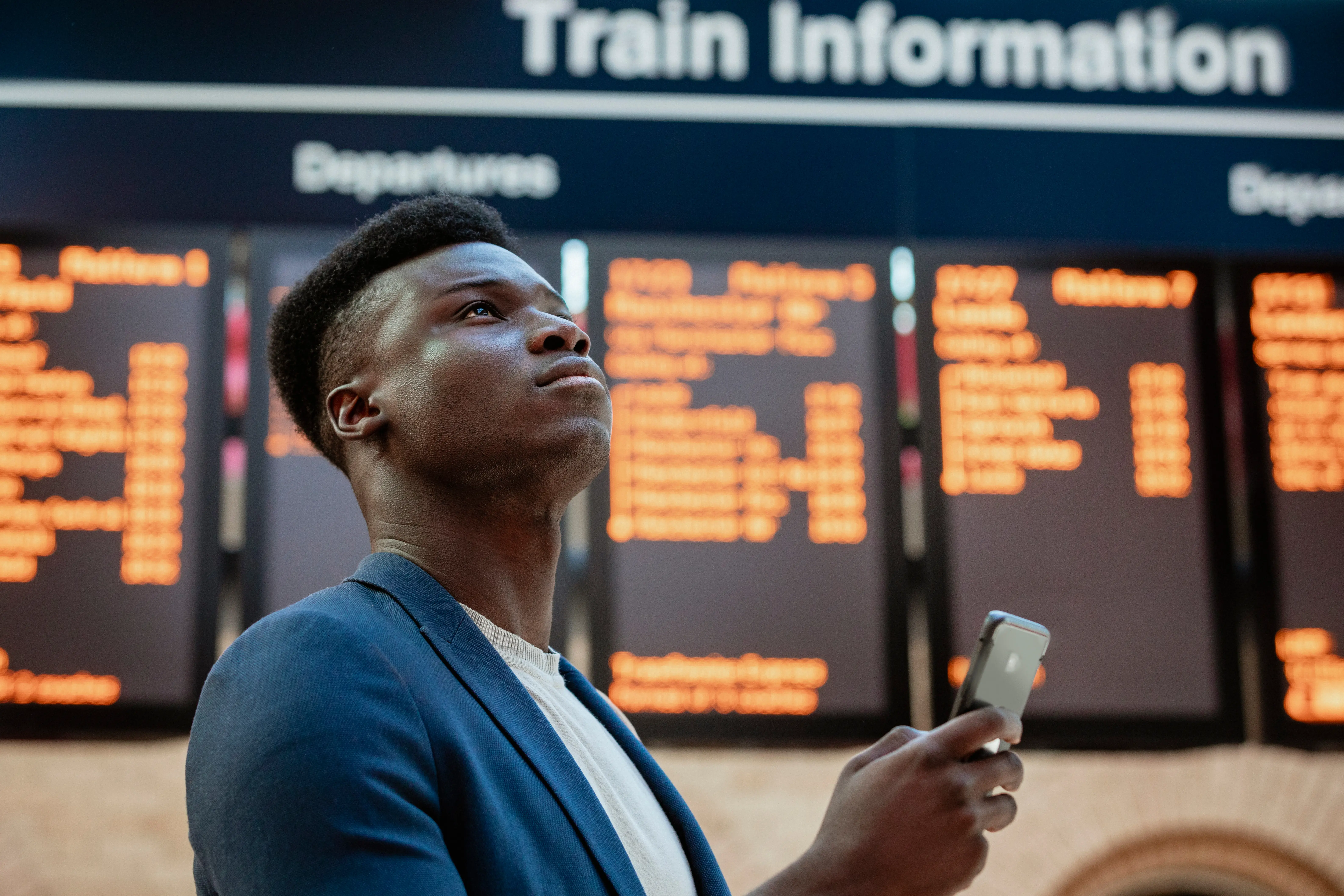 Train Departure Boards: A young businessman holding his phone looks up at an off-screen departure board or time table