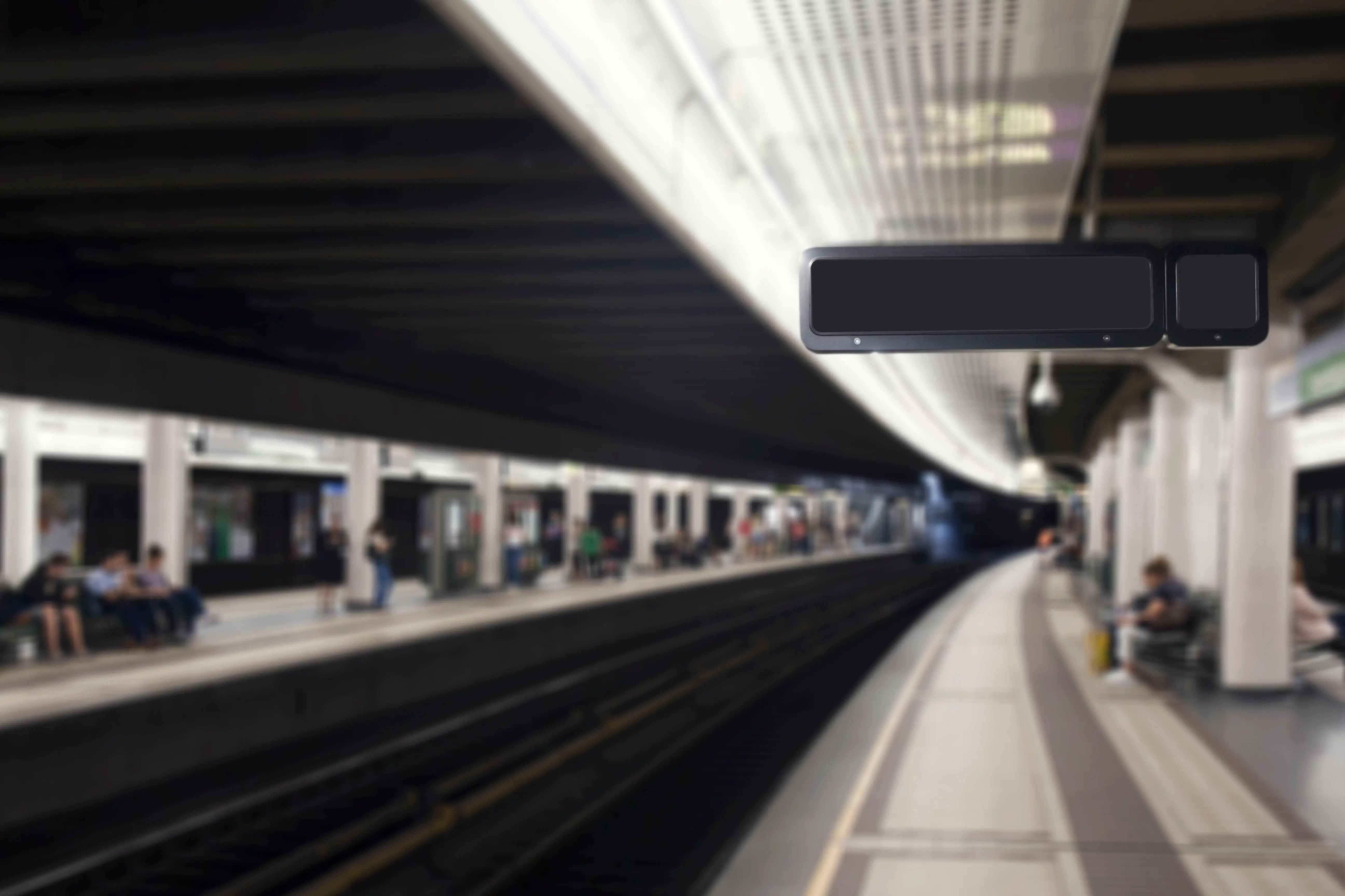 Train Departure Boards: A slightly blurry photo of an underground train station, showing a few people sat or stood around, and a blank display board above a platform
