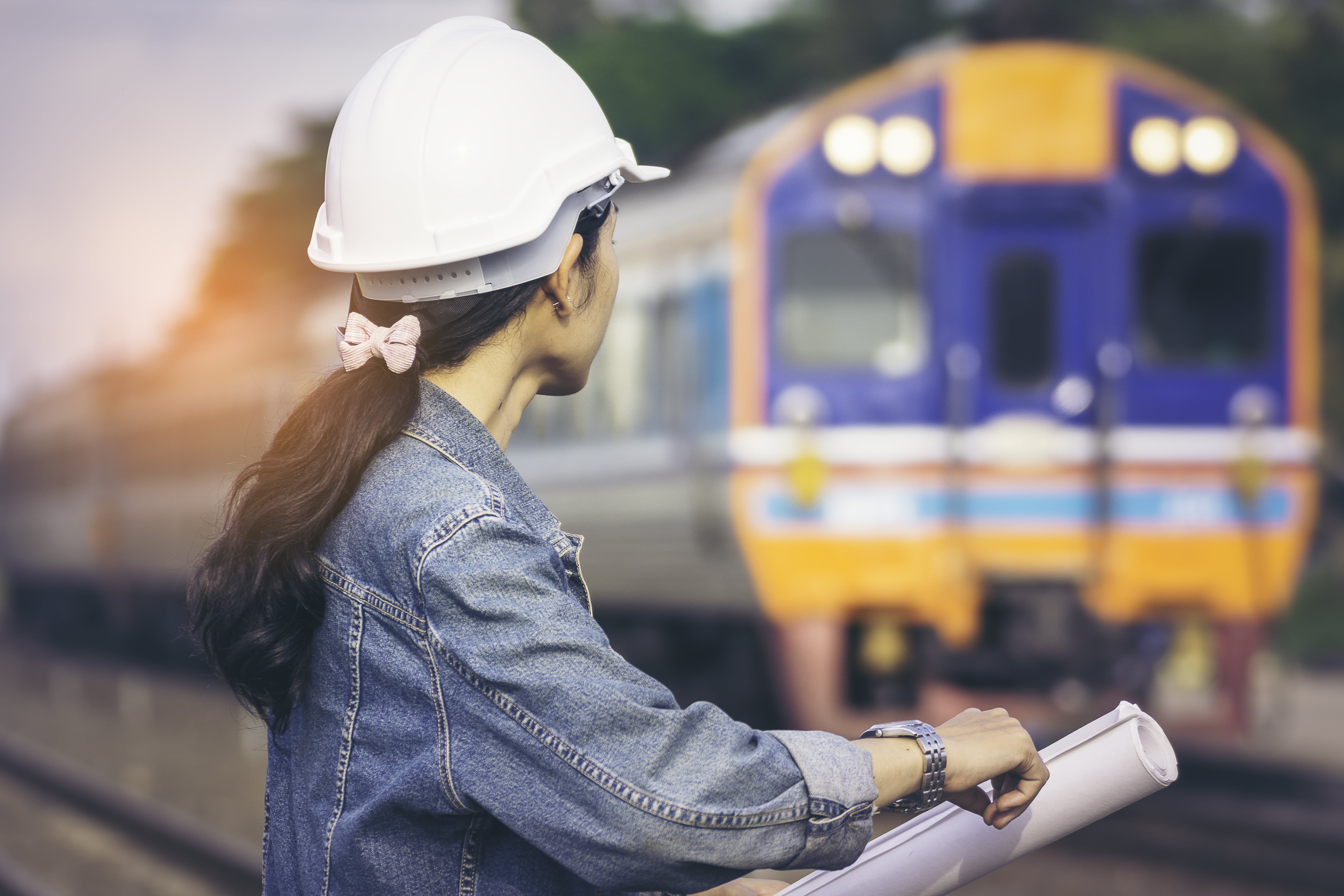 Women in Rail: A smartly dressed female train conductor wearing a red kerchief leans against a train seat.