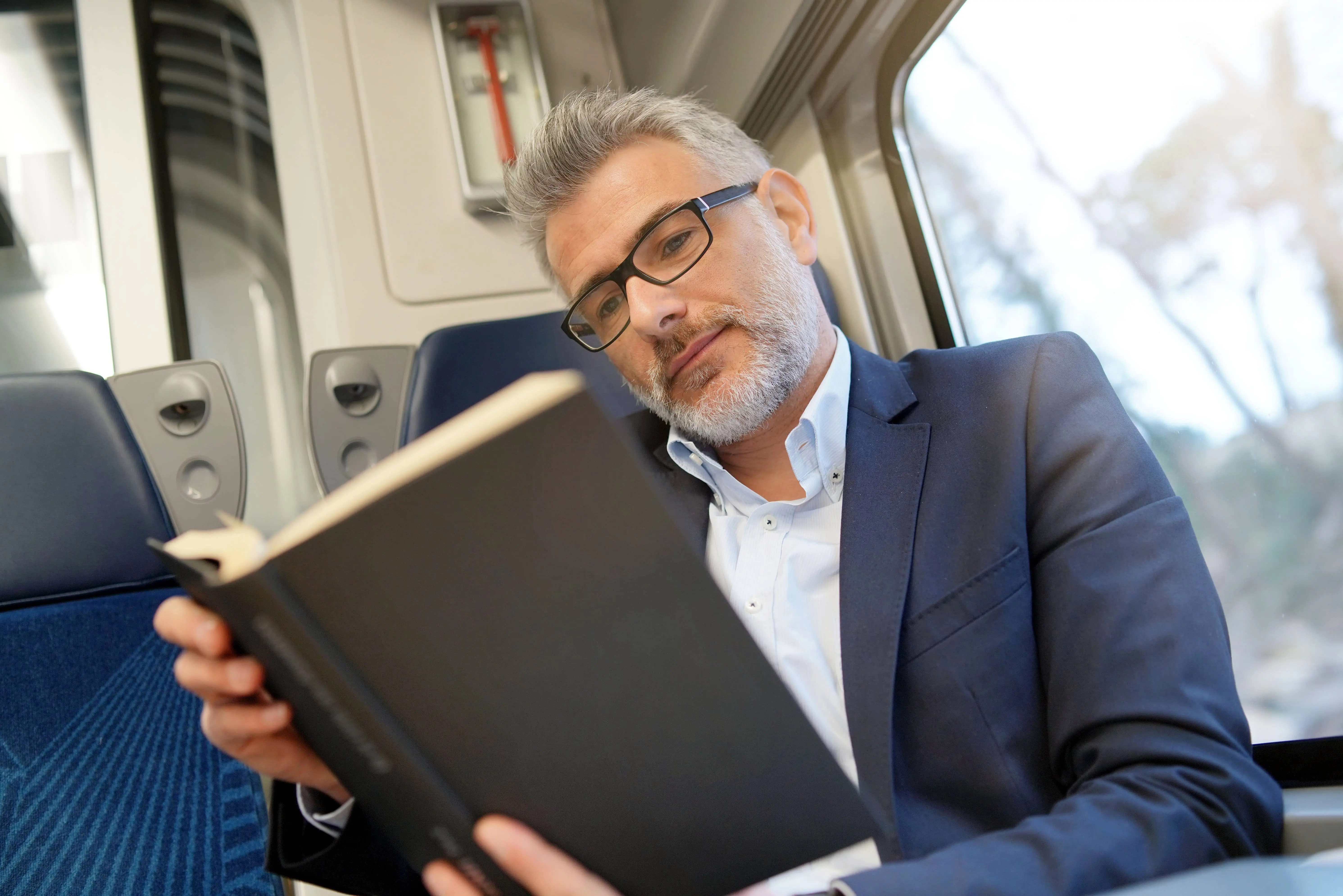 Train Literature: A man sat on a train reading a book.