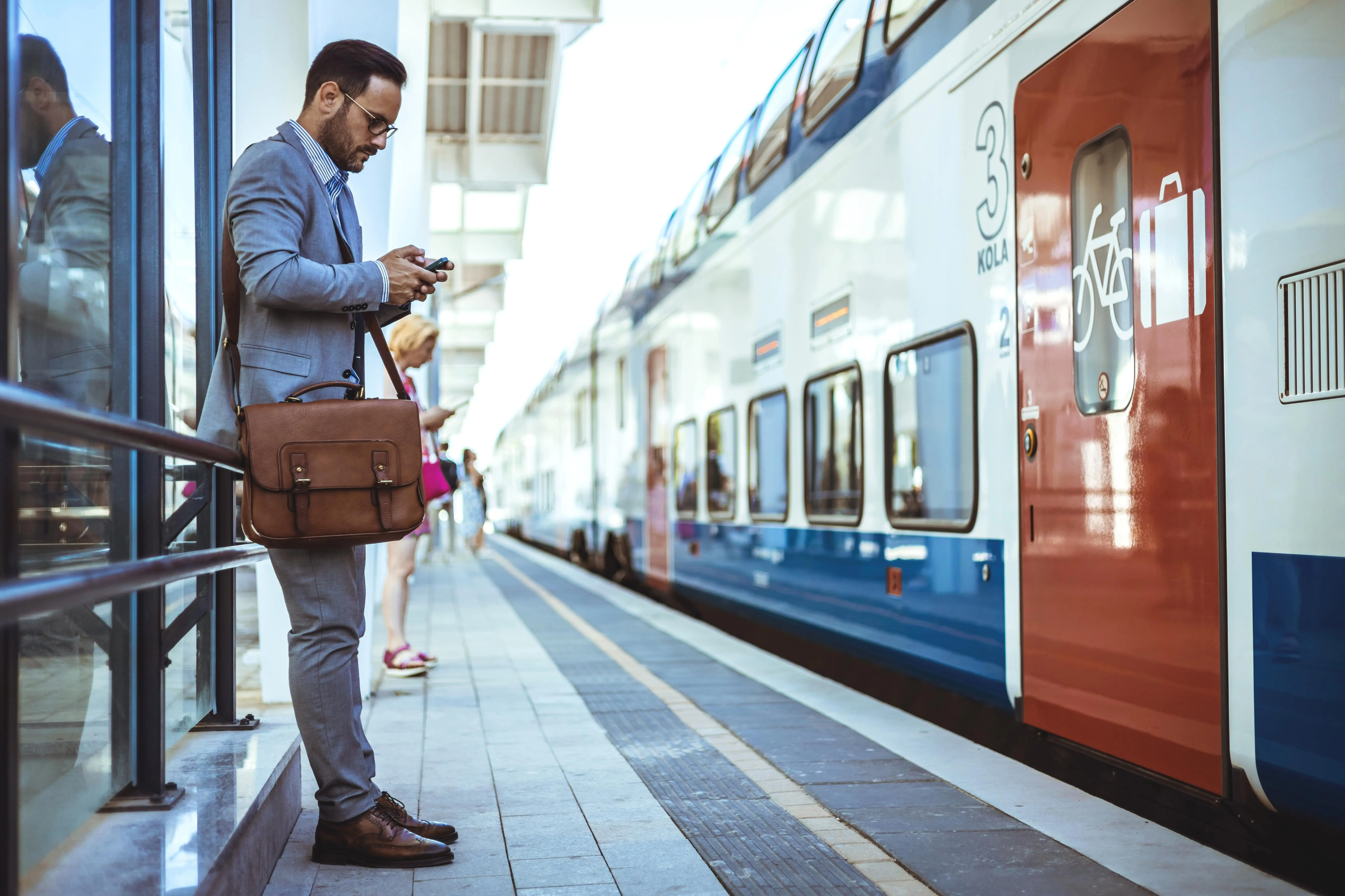 A suited man prepares to board a train whilst checking his phone
